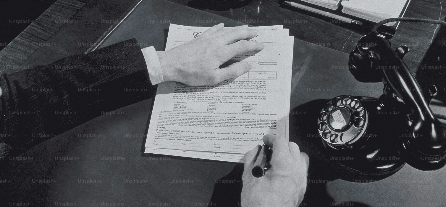 Photographie en noir et blanc d’une main en train d’écrire des notes sur papier, sur un bureau.